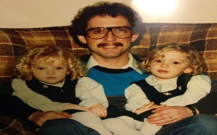 Leah Gibson's childhood photo in a white baby gown and black top with her twin sister and her father.